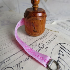 May include: A wooden measuring tape with a pink ribbon and a silver ring. The tape is labeled "Brown's" and has a wooden knob.