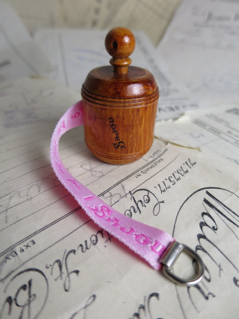 May include: A wooden measuring tape with a pink ribbon and a silver ring. The tape is labeled "Brown's" and has a wooden knob.