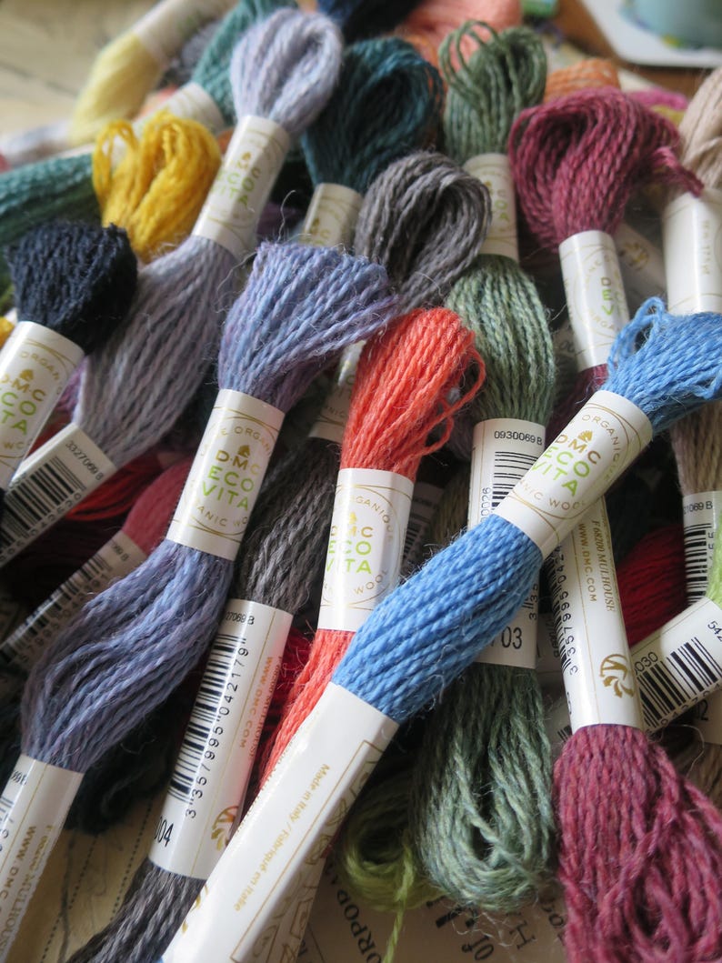 May include: A collection of DMC Eco Vita embroidery floss spools in various colors, including blue, green, red, and yellow. The spools are labeled with the DMC Eco Vita logo and the color number.
