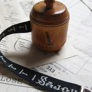 May include: A wooden spool with a knob on top and a black ribbon with white lettering that reads "UN JOJOU 1 177 SAJOU".