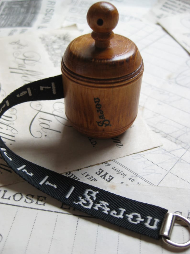 May include: A wooden spool with a knob on top and a black ribbon with white lettering that reads "UN JOJOU 1 177 SAJOU".