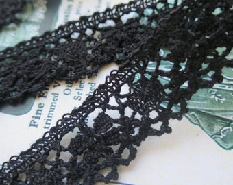 Puede incluir: Borde de encaje negro con un delicado patrón floral. El borde está hecho de un material fino y suave y tiene una superficie ligeramente texturizada.