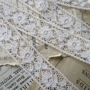 May include: White cotton lace trim with a delicate floral pattern. The lace is approximately 1/2 inch wide.
