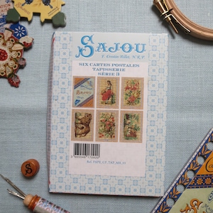 May include: A rectangular Sajou product package featuring a light blue patterned border and a central white label with the text Six Cartes Postales Tapisserie Série 3, displaying six small needlepoint-style images and a barcode at the bottom.