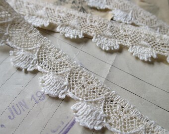 May include: White cotton lace trim with a delicate scalloped edge. The lace has a repeating pattern of small circles and a larger, fan-shaped design.