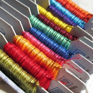 May include: A close-up of a variety of embroidery floss spools in a white plastic organizer. The floss is arranged in rows of different colors, including red, orange, yellow, green, blue, purple, and brown.