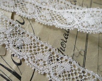 May include: White cotton lace trim with a delicate floral pattern. The lace is approximately 1/2 inch wide.