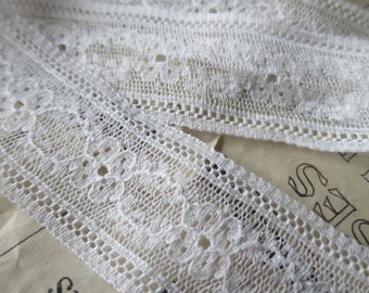May include: White lace trim with a delicate floral pattern. The lace is approximately 1 inch wide and has a scalloped edge.