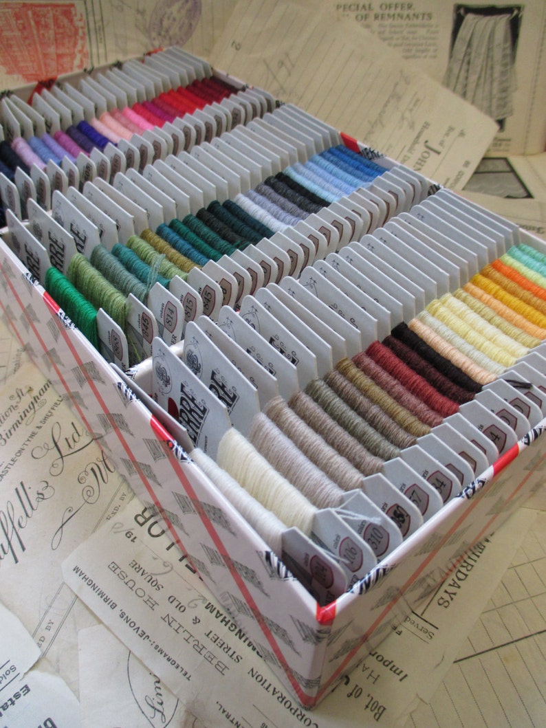 May include: A white box filled with spools of embroidery floss in various colors. The box is labeled "J. & J.  Lud.  Ltd."