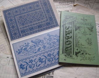 Può includere: Un libretto verde con il titolo "Dessins de Broderies" e il numero 657. Il libretto è aperto per mostrare una pagina con un disegno floreale e il testo "SAJOU" in grandi lettere. Il libretto è sopra una pila di fogli con un motivo di ricamo blu e bianco.