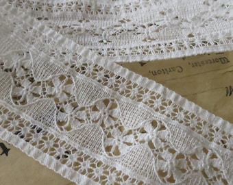 May include: White cotton lace trim with a delicate floral pattern. The lace is approximately 1 inch wide and has a scalloped edge.