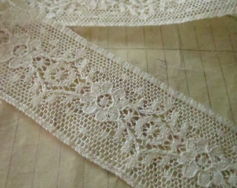 May include: White lace trim featuring a delicate floral design. The lace is made from a fine, lightweight fabric and has a soft, flowing texture.