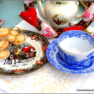Könnte beinhalten: Eine weiße Teetasse und Untertasse mit einem blauen und weißen Blumenmuster. Die Teetasse ist mit weißer Flüssigkeit gefüllt. Die Untertasse steht auf einer weißen Tischdecke mit einem mehrstöckigen Ständer mit Mini-Torten.