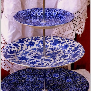 Könnte beinhalten: Ein dreistöckiger Kuchenständer mit einem silbernen Ständer und blauen und weißen floralen Tellern.