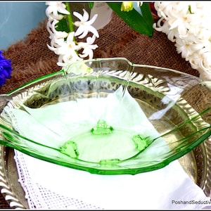 Può includere: Una ciotola da portata in vetro verde vintage con un bordo scanalato. La ciotola è appoggiata su un vassoio d'argento con un motivo decorativo.