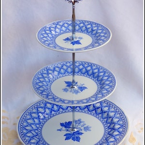 May include: A three-tiered cake stand with a silver stand and blue and white porcelain plates. The plates have a floral design with blue and white accents.