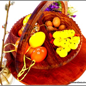 May include: A wooden basket with a handle, divided into sections. The basket contains yellow and orange Easter eggs, walnuts, and yellow chicks. The basket is sitting on a wooden surface.