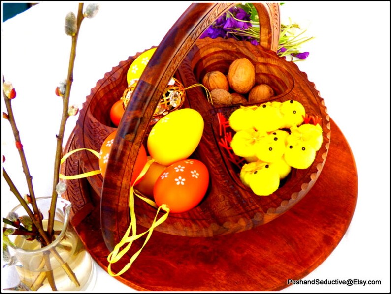 May include: A wooden basket with a handle, divided into sections. The basket contains yellow and orange Easter eggs, walnuts, and yellow chicks. The basket is sitting on a wooden surface.