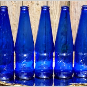 May include: Five cobalt blue glass bottles with the numbers 4 and 6 embossed on them. The bottles are arranged in a row on a silver tray.