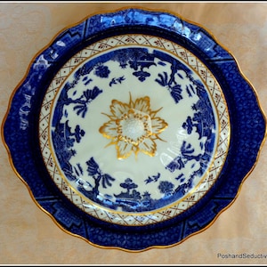Peut inclure: Un plat de service en porcelaine bleu et blanc avec un motif floral doré au centre. Le plat a un bord festonné et un motif bleu et blanc autour du bord.