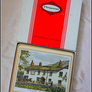 Peut inclure: Un ensemble de six sets de table traditionnels dans une boîte. La boîte est blanche avec un panneau rouge portant la marque "Pimpernel". Les sets de table représentent une illustration détaillée d'un bâtiment avec une calèche et le texte "The Swan - Grasmere".