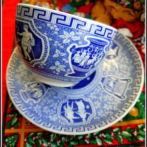 Könnte beinhalten: Eine blaue und weiße Porzellan-Teetasse und -Untertasse mit einem griechischen Schlüsselmuster und einem floralen Muster. Tasse und Untertasse zeigen eine Szene mit Menschen in einem Garten.