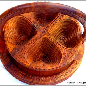 May include: A wooden serving tray with four heart-shaped compartments. The tray has a handle and is intricately carved with floral designs.