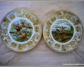 May include: Two white ceramic plates with gold trim and a hunting scene in the center. The plates feature a detailed floral design around the edge.