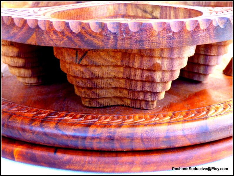 May include: A wooden serving tray with two carved bowls. The tray is made of dark wood with a reddish hue and has a decorative carved border. The bowls are also made of dark wood and have a layered, tiered design.