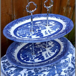May include: Two-tiered serving stand made from blue and white china with a silver stand. The stand features a traditional willow pattern.
