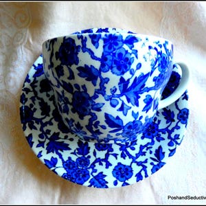 Könnte beinhalten: Eine weiße Teetasse und Untertasse mit einem blauen Blumenmuster. Das Muster zeigt blaue Blumen und Blätter auf weißem Hintergrund.