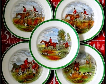 May include: Five white ceramic plates with a green scalloped edge. Each plate features a detailed illustration of a fox hunt scene with riders in red coats on horseback, dogs, and a landscape background.
