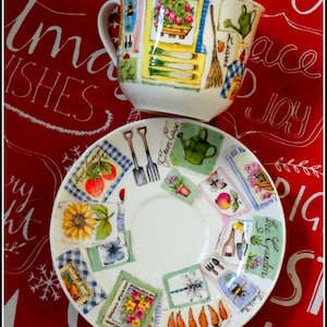 May include: A white ceramic teacup and saucer set with a garden theme. The cup and saucer feature colorful illustrations of gardening tools, flowers, vegetables, and insects. The set is decorated with a mix of square and rectangular images.