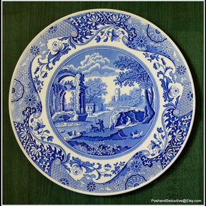 May include: A blue and white ceramic plate with a floral border and a central image of a landscape with a castle and ruins. The plate is decorated in a traditional blue and white pattern.