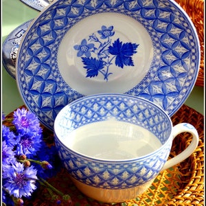 May include: A blue and white teacup and saucer set with a floral design. The saucer has a geometric pattern around the edge. The teacup and saucer are sitting on a woven wicker surface.