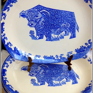 May include: A set of four blue and white ceramic plates featuring a stylised design of a cow. The plates have a white background with a blue border and a blue cow design in the centre.