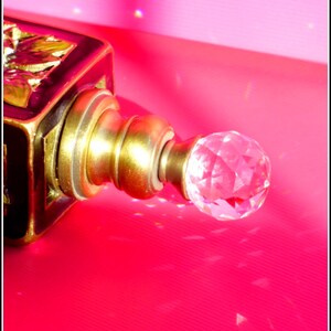 May include: A black and gold bottle stopper with a crystal-like knob. The stopper is on a pink surface.