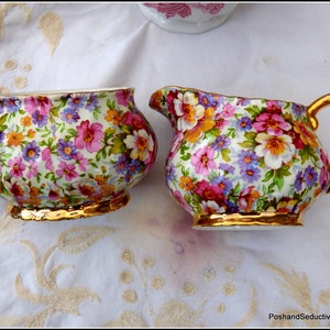 以下が含まれることがあります： 金色の縁取りが施された、ヴィンテージのフローラル柄のシュガーボウルとクリーマーのセット。セットは白い磁器製で、ピンク、パープル、イエローの繊細な花柄が特徴です。