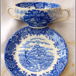 Può includere: Un set da tè in porcellana blu e bianca con una scena di cottage. La tazza e il piattino presentano un motivo floreale blu e bianco.