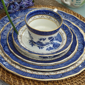 Puede incluir: Un juego de cuatro platos de porcelana azul y blanco con ribetes dorados, con un diseño chino tradicional. Los platos están apilados, con una taza de té y un platillo a juego en la parte superior.