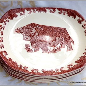 May include: A stack of oval serving platters. Each plate has a cream base and a brown bull illustration. The plates feature a decorative border with floral and animal motifs. The bull is depicted with intricate patterns and a flower.