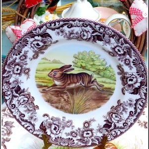 Könnte beinhalten: Ein antiker violetter und weißer Porzellanteller mit Blumenmuster und einem gemalten Bild eines braunen Kaninchens auf einer Wiese.