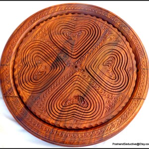 May include: A round wooden serving tray with a carved design of four hearts. The tray is made of dark brown wood and has a smooth finish.