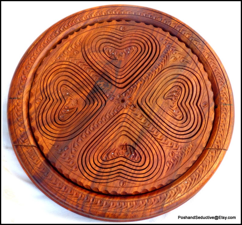 May include: A round wooden serving tray with a carved design of four hearts. The tray is made of dark brown wood and has a smooth finish.