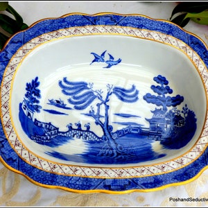May include: A blue and white oval serving dish with a willow pattern design. The dish has a gold rim and a scalloped edge.