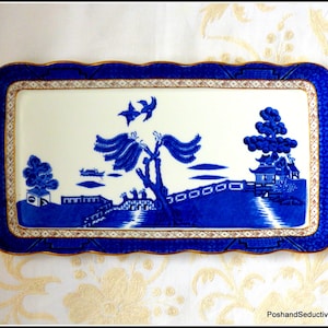 May include: A blue and white rectangular serving tray with a gold trim and a traditional Chinese landscape design. The tray has a scalloped edge.