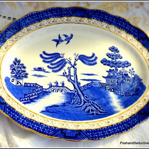 May include: A blue and white oval serving platter with a traditional willow pattern design. The platter features a gold trim and a scalloped edge.