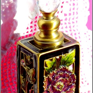 May include: A black and gold perfume bottle with a crystal stopper. The bottle is decorated with a purple flower and green leaves.