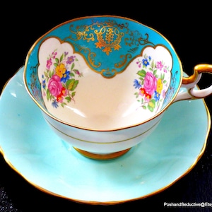 May include: A vintage teacup and saucer set with a turquoise blue and gold design. The cup features a white interior with floral accents and a gold rim. The saucer has a matching turquoise blue color with a gold rim.