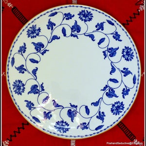May include: A white ceramic plate with a blue and white floral design. The plate has a gold rim and is decorated with a repeating pattern of stylized flowers and leaves.